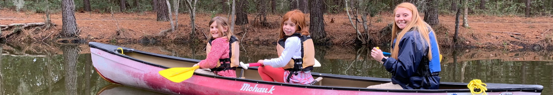 Two campers and a camp counselor canoe in a creek