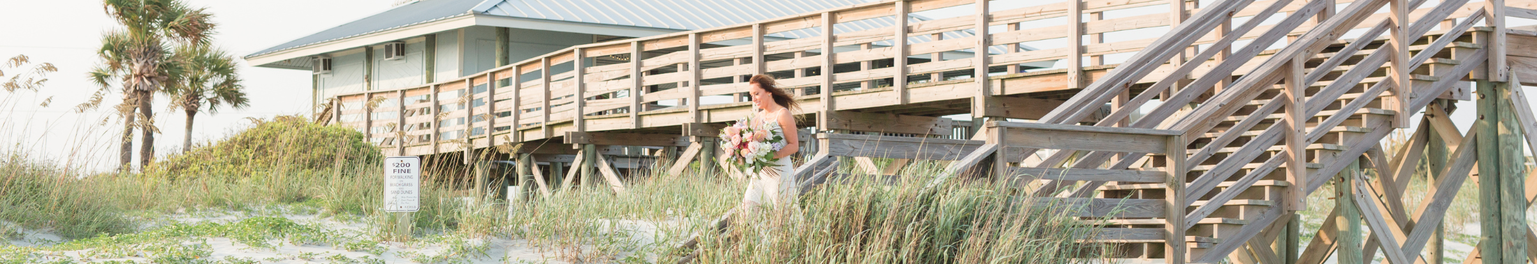 A bride walks down the boardwalk to the beach towards her wedding ceremony. 
