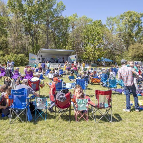 People in lawn chairs in the park listening to a band on stage